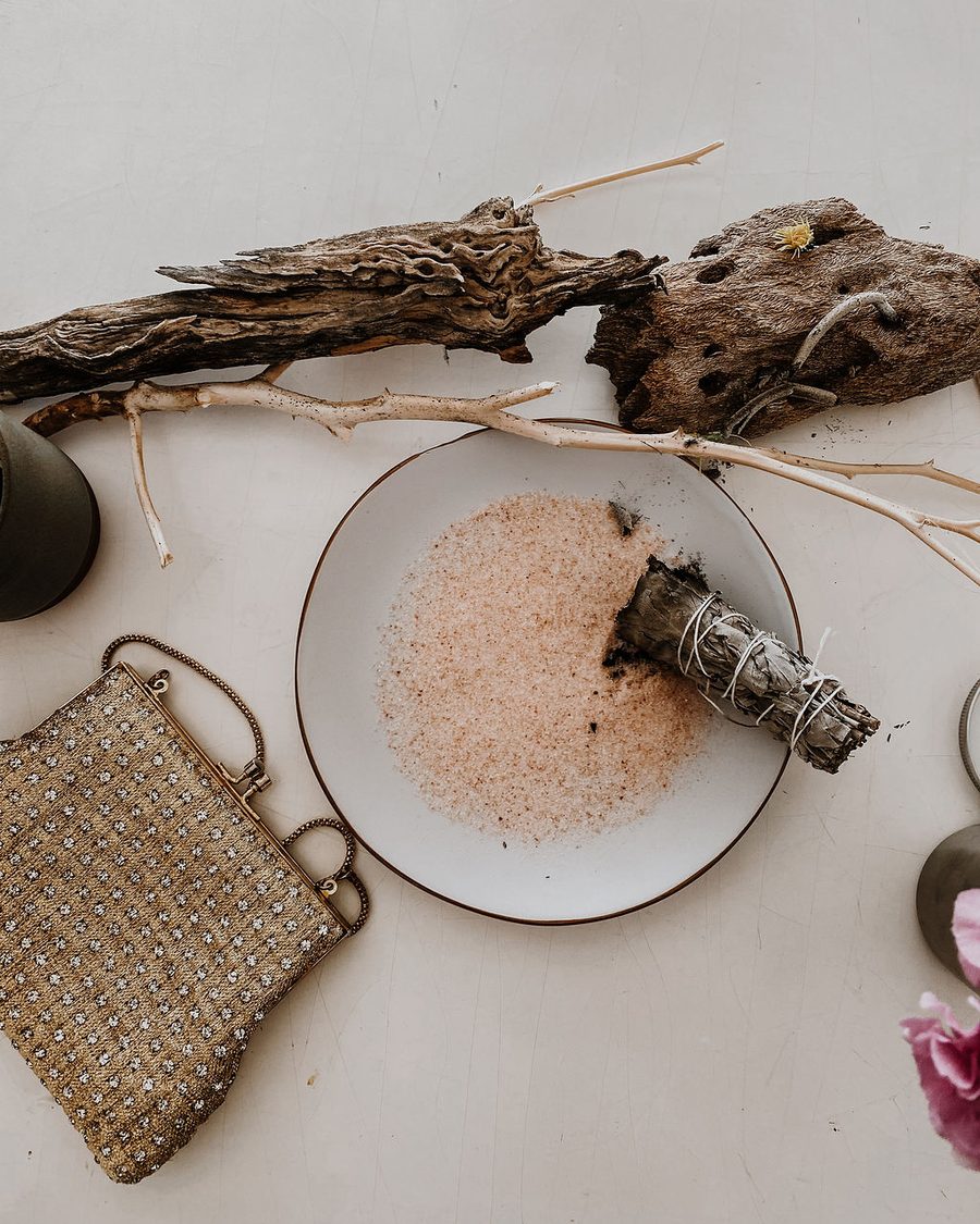 A sage bundle resting on a plate of pink salt beside driftwood